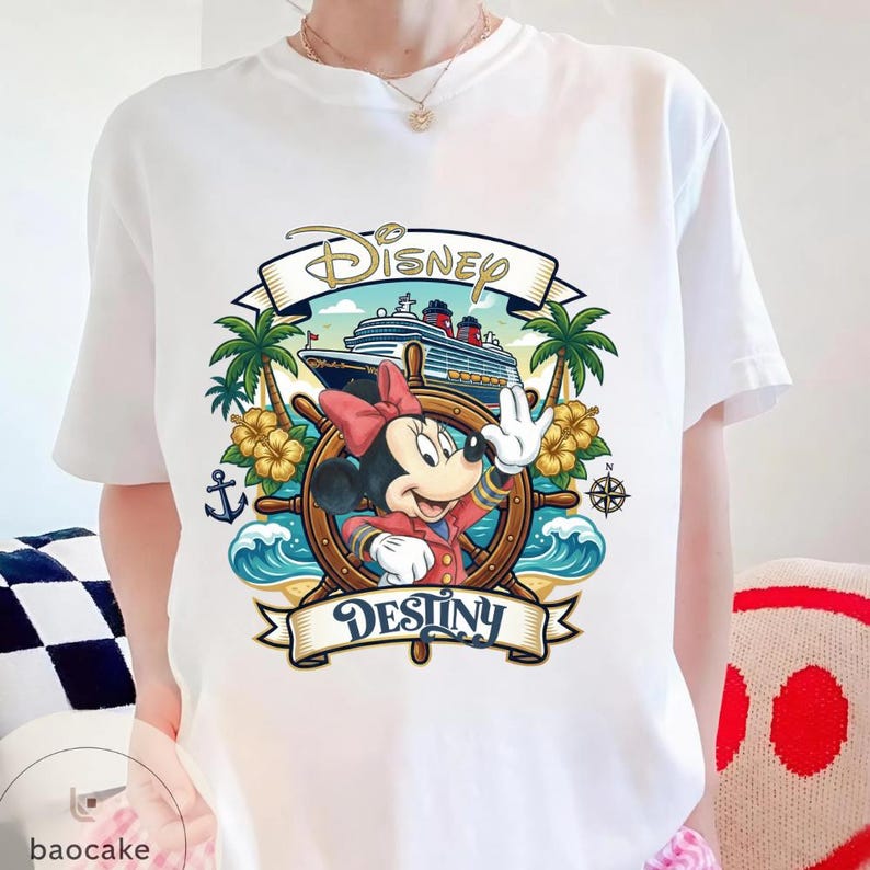 May include: White t-shirt featuring a colorful graphic of Minnie Mouse waving from a ship's wheel. The design includes a cruise ship, palm trees, and the words "Disney Destiny". The shirt is a crew neck style.