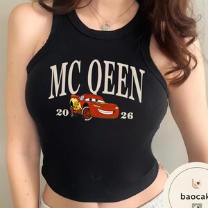May include: Black tank top with the text "MC QUEEN" in white, featuring a cartoon image of a red race car. The numbers "20" and "26" are printed on either side of the car. A casual, sleeveless top.