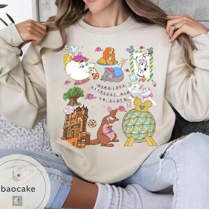 May include: Beige sweatshirt with colorful cartoon illustrations of Disney characters and landmarks. The design includes a teapot, dogs, cats, a kangaroo, and the text "Mom Vibes Happiest Mom on Earth."