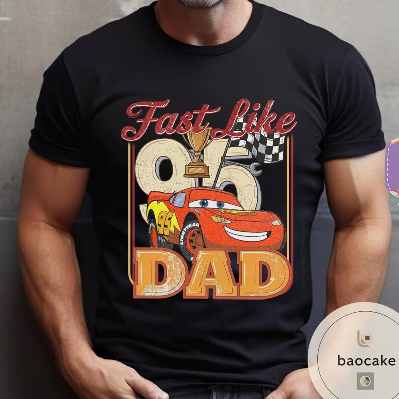 May include: Black t-shirt with a graphic featuring a red race car, a trophy, and the text "Fast Like Dad." The design includes the number 95 and a checkered flag, creating a racing theme.