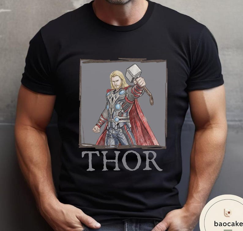 May include: Black t-shirt featuring a graphic of Thor, a superhero with blonde hair, holding a hammer. The image is framed in a gray box, with the name "THOR" printed below in a serif font.