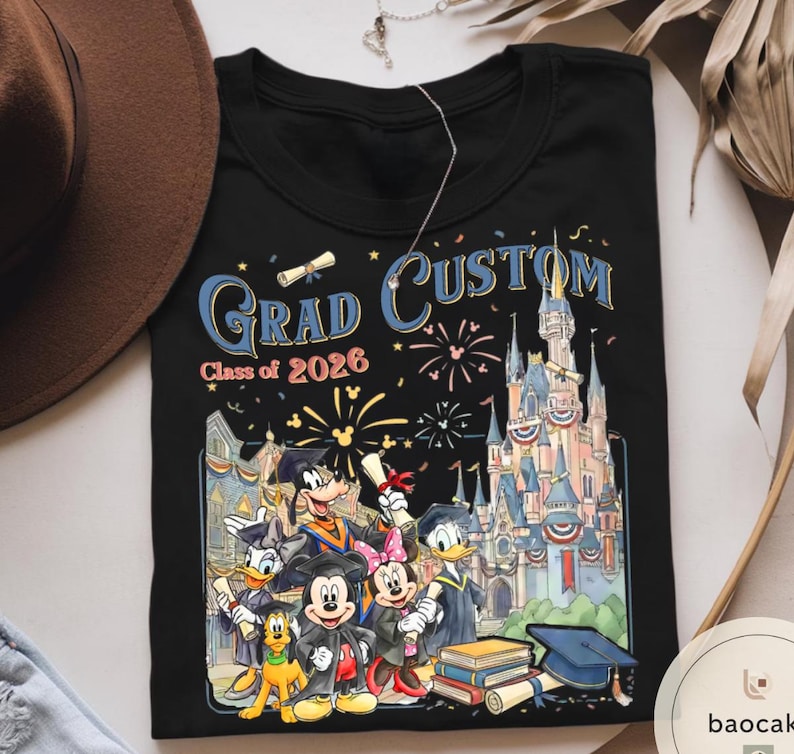 May include: Black t-shirt with a colourful graphic of Disney characters in graduation attire, with the words "Grad Custom Class of 2026". The design includes a castle, fireworks, and graduation caps.