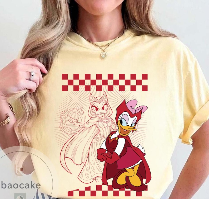 May include: Yellow t-shirt featuring a red and white checkered pattern and a graphic of two cartoon characters. One character is a duck in a red outfit with a pink bow. The other is a duck in a red and white outfit.