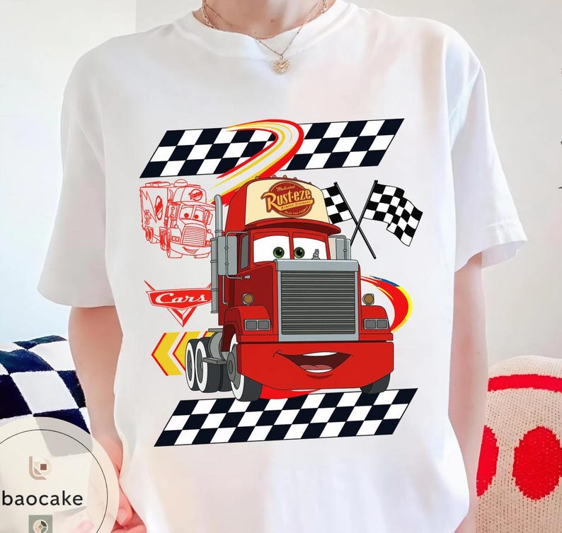 May include: White t-shirt featuring a cartoon image of the character Mack from the movie Cars. The design includes a red truck with the text "Rust-eze" on the cap, checkered flags, and the word "Cars".