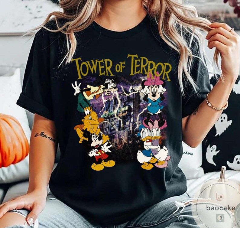May include: Black t-shirt featuring the text "Tower of Terror" in gold lettering. The graphic includes cartoon characters like Mickey Mouse, Minnie Mouse, Donald Duck, and Goofy, with a background of a building and lightning.