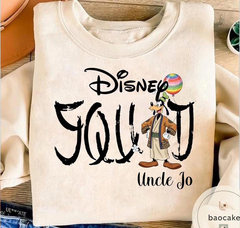 Puede incluir: Sudadera color crema con el texto "Disney Squad" en escritura negra, con un personaje de dibujos animados de Goofy sosteniendo un globo de arco&iacute;ris. Las palabras "Uncle Jo" est&aacute;n impresas debajo.