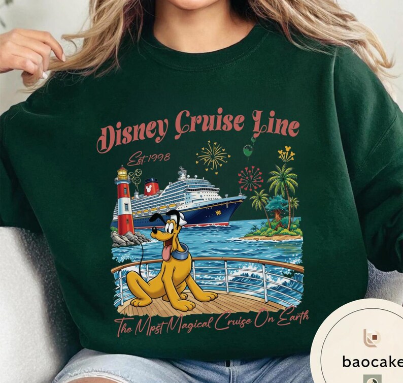 K&ouml;nnte beinhalten: Dunkelgr&uuml;nes Sweatshirt mit einem Disney Cruise Line-Motiv. Das Design zeigt ein Kreuzfahrtschiff, Pluto den Hund, einen Leuchtturm und eine tropische Landschaft. Der Text lautet "Disney Cruise Line Est. 1998" und "The Most Magical Cruise On Earth."