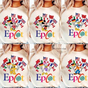 May include: A cream-coloured sweatshirt with a colourful graphic of Disney characters holding flags from around the world. The word "Epcot" is written in blue, orange, and red, with a globe graphic. The sweatshirt is a casual style.