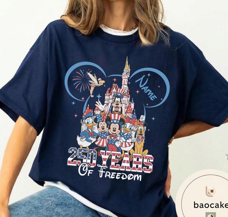 Peut inclure: T-shirt bleu marine avec un motif color&eacute; de personnages Disney en tenue patriotique devant un ch&acirc;teau. Le motif comprend le texte "250 Years Of Freedom" et un espace pour un nom. Le t-shirt a des manches courtes et un col rond.
