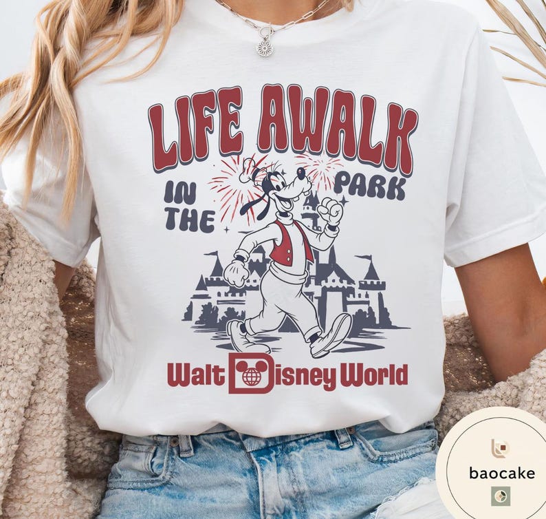 May include: White t-shirt featuring a graphic of Goofy running in front of a castle, with the text "LIFE A WALK IN THE PARK" and "Walt Disney World" in red and black.