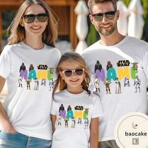 May include: White t-shirts with a Star Wars theme. Each shirt features the text "NAME" in colorful letters, surrounded by Star Wars characters. The shirts are worn by a family of three.