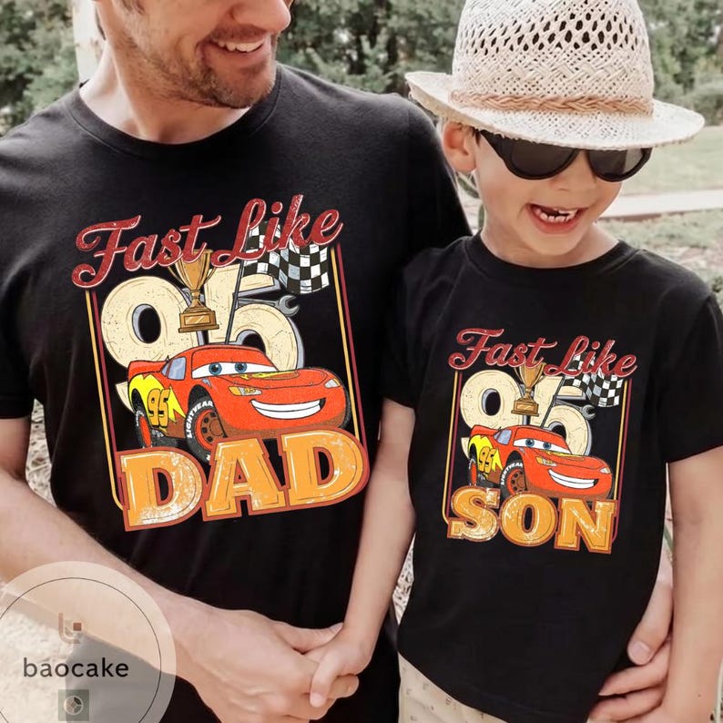 May include: Black t-shirts with a cartoon car graphic. One shirt says "Fast Like Dad" and the other says "Fast Like Son". The graphic includes a trophy, checkered flag, and the number 95.