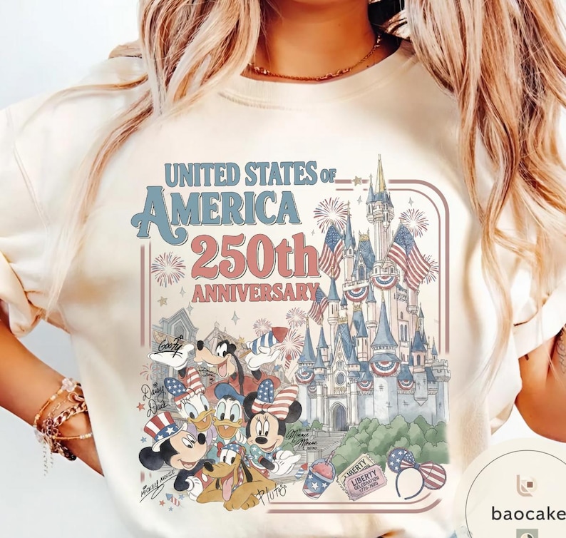May include: Cream-colored t-shirt featuring a graphic celebrating the 250th anniversary of the United States of America. The design includes a castle, fireworks, and Disney characters like Mickey and Minnie Mouse, all in patriotic colors.