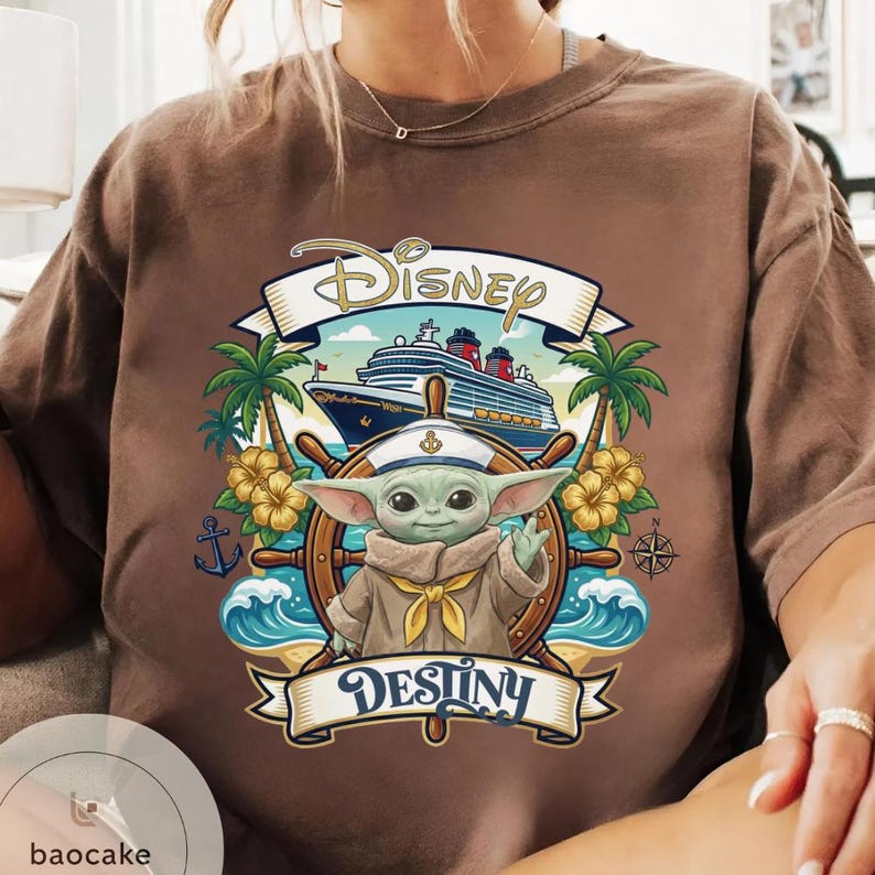 May include: Brown t-shirt featuring a graphic of Baby Yoda at the helm of a ship with the word "Disney" above and "Destiny" below. The design includes palm trees, waves, and a cruise ship.