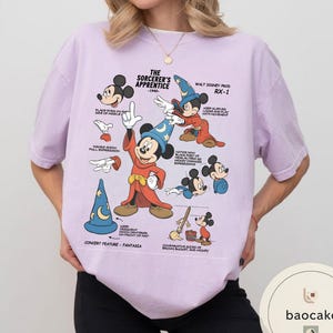 May include: A light purple t-shirt featuring a graphic of Mickey Mouse in his Sorcerer's Apprentice attire. The design includes various poses and text from the 1940s film, with the words "The Sorcerer's Apprentice" and "Walt Disney Prod RX-1".