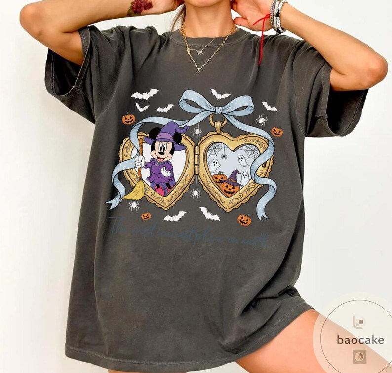 May include: Dark grey t-shirt with a heart-shaped locket design featuring Mickey Mouse in a witch costume and Halloween illustrations. The locket has a blue ribbon, bats, spiders, and pumpkins. The text "...a castle" is visible.