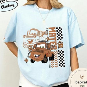 May include: Pale blue t-shirt with a brown cartoon tow truck design and the word "MATEr" in a vertical block. The design includes a checkered flag pattern and the text "Chambray" in a circular design.