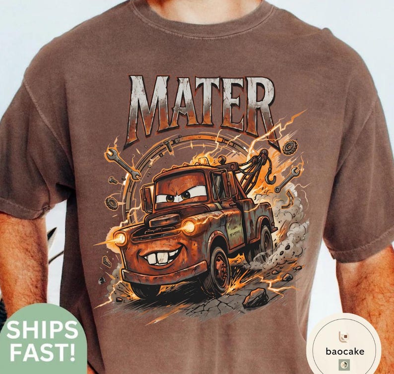 May include: Brown t-shirt with a cartoon image of Mater from the Cars film. The graphic includes the word "MATER" in a distressed font, with lightning bolts and tools. The tow truck Mater is smiling and has his headlights on.