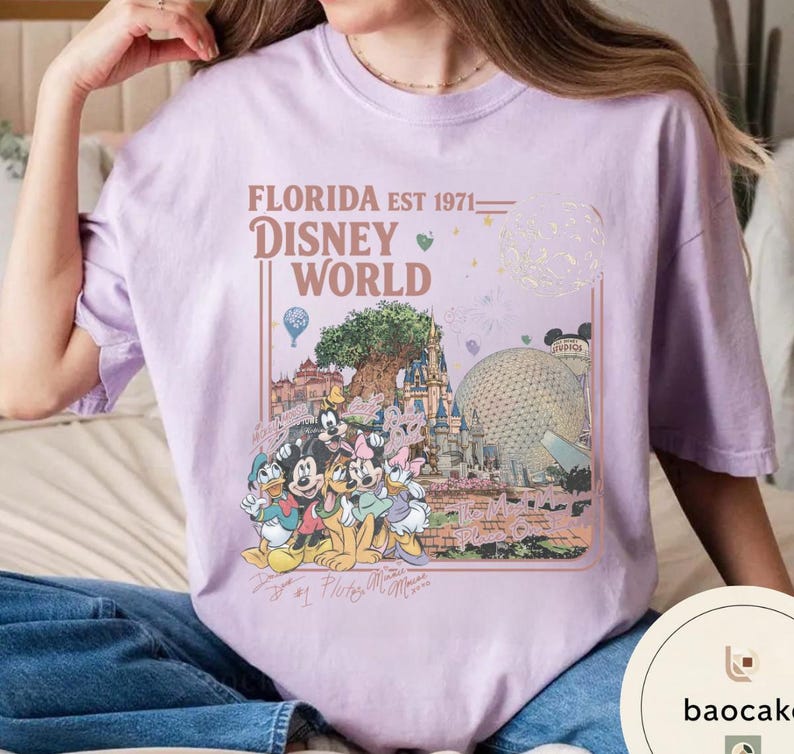 May include: A light purple t-shirt featuring a graphic print of Disney World landmarks and characters. The text reads FLORIDA EST 1971 DISNEY WORLD. The design includes Mickey Mouse, Minnie Mouse, Donald Duck, Daisy Duck, and Pluto, along with the Tree of Life and Epcot sphere.