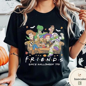 May include: A black t-shirt featuring a graphic print of Toy Story characters sitting on a couch with Halloween elements like bats and leaves. The text reads F R I E N D S SINCE HALLOWEEN 1995. The design includes Woody, Buzz Lightyear, Jessie, Rex, Bullseye, and Mr. Potato Head.