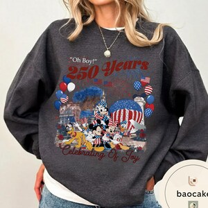 Puede incluir: Sudadera gris oscuro con un gr&aacute;fico colorido que celebra 250 a&ntilde;os. El dise&ntilde;o incluye fuegos artificiales, globos y personajes de Disney. El texto incluye "Oh Boy!" y "Celebrating of Joy."