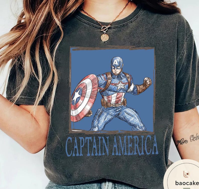 May include: Dark gray t-shirt featuring a Captain America graphic. The design shows Captain America in a blue and red costume with his shield, set against a blue background. The words "CAPTAIN AMERICA" are printed below the image.