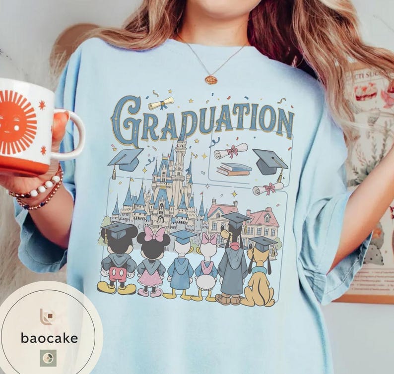 May include: Light blue t-shirt with the word "Graduation" in a vintage font, featuring a Disney castle and cartoon characters in graduation attire. The shirt includes a coffee mug with a sun design.