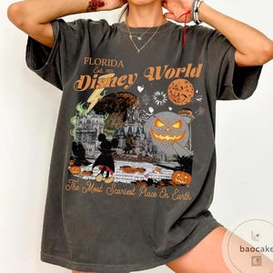 May include: Dark gray t-shirt with a Halloween-themed Disney World graphic. The design includes a castle, Mickey Mouse, pumpkins, and the text "Florida Disney World" and "The Most Scariest Place On Earth."