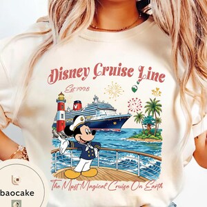 K&ouml;nnte beinhalten: Cremefarbenes T-Shirt mit einem Disney Cruise Line-Motiv. Das Design zeigt ein Kreuzfahrtschiff, Mickey Mouse in Kapit&auml;nsuniform, einen Leuchtturm und den Text "Disney Cruise Line Est. 1998" und "The Most Magical Cruise On Earth."