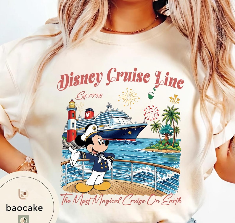 K&ouml;nnte beinhalten: Cremefarbenes T-Shirt mit einem Disney Cruise Line-Motiv. Das Design zeigt ein Kreuzfahrtschiff, Mickey Mouse in Kapit&auml;nsuniform, einen Leuchtturm und den Text "Disney Cruise Line Est. 1998" und "The Most Magical Cruise On Earth."