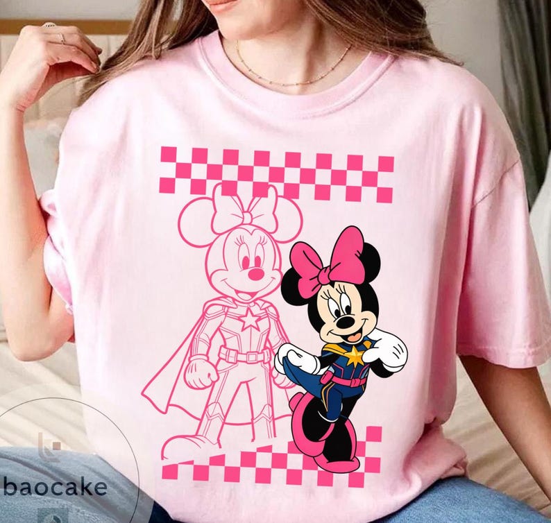 May include: Pink t-shirt featuring a graphic of Minnie Mouse in two different styles. One is a pink outline, and the other is a full-color image of Minnie Mouse in a superhero outfit. The shirt has a pink and white checkered pattern.