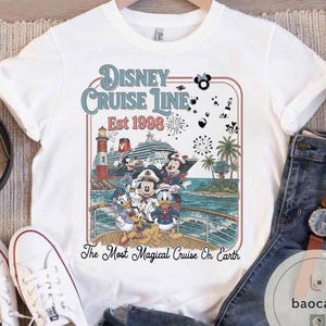 Puede incluir: Camiseta blanca con un gr&aacute;fico colorido de personajes de Disney en un crucero. El dise&ntilde;o incluye el texto "Disney Cruise Line Est 1998" y "The Most Magical Cruise On Earth". La camiseta tiene cuello redondo y mangas cortas.
