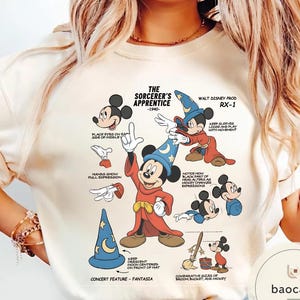 May include: Cream-colored t-shirt featuring a graphic of Mickey Mouse in his Sorcerer's Apprentice attire. The design includes illustrations and text detailing the character's features and the film's production notes. The text includes "The Sorcerer's Apprentice -1940-" and "Walt Disney Prod RX-1".