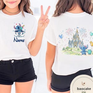 May include: White t-shirts with cartoon graphics. One shirt features a blue character in a teacup with the name "Name". The other shirt displays a castle, fireworks, and a blue character with a green friend.