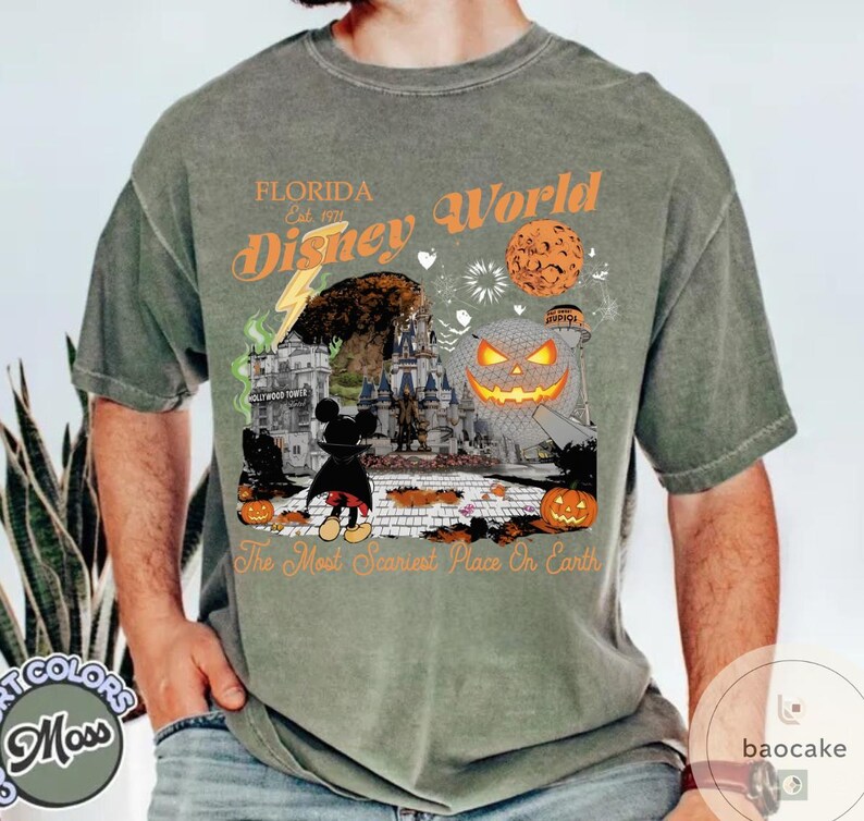 May include: Moss green t-shirt featuring a Halloween-themed Disney World graphic. The design includes a castle, Mickey Mouse, pumpkins, and the text "Florida Disney World" and "The Most Scariest Place On Earth."