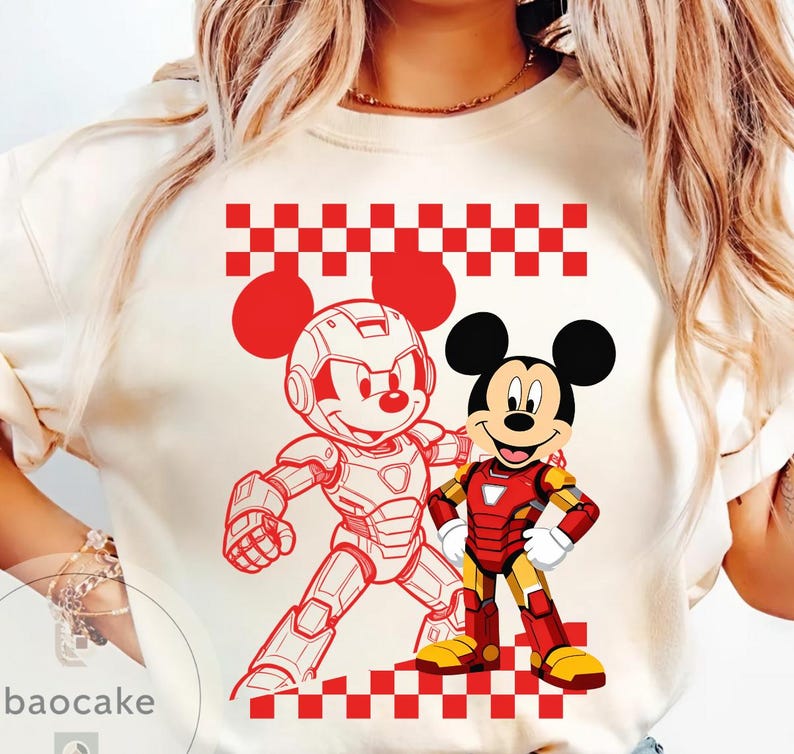 May include: Cream-colored t-shirt featuring a red and white checkered pattern and two Mickey Mouse illustrations. One Mickey is in a robotic suit, and the other is in an Iron Man suit. The shirt has a crew neck.