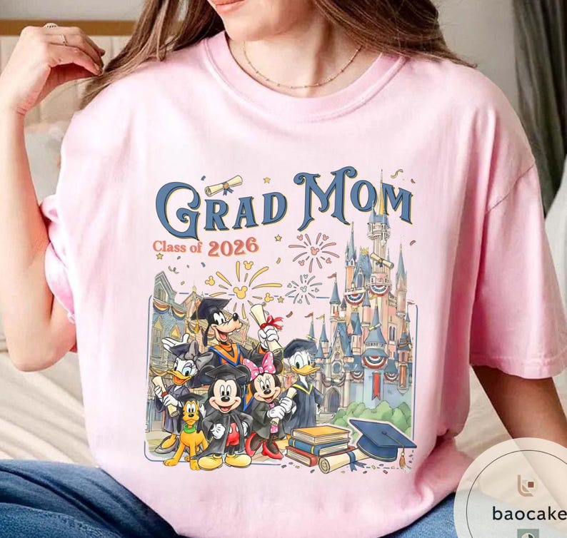 May include: Pale pink t-shirt with the words "Grad Mom" in blue script, and "Class of 2026" in smaller text. The graphic features Disney characters in graduation attire in front of a castle.