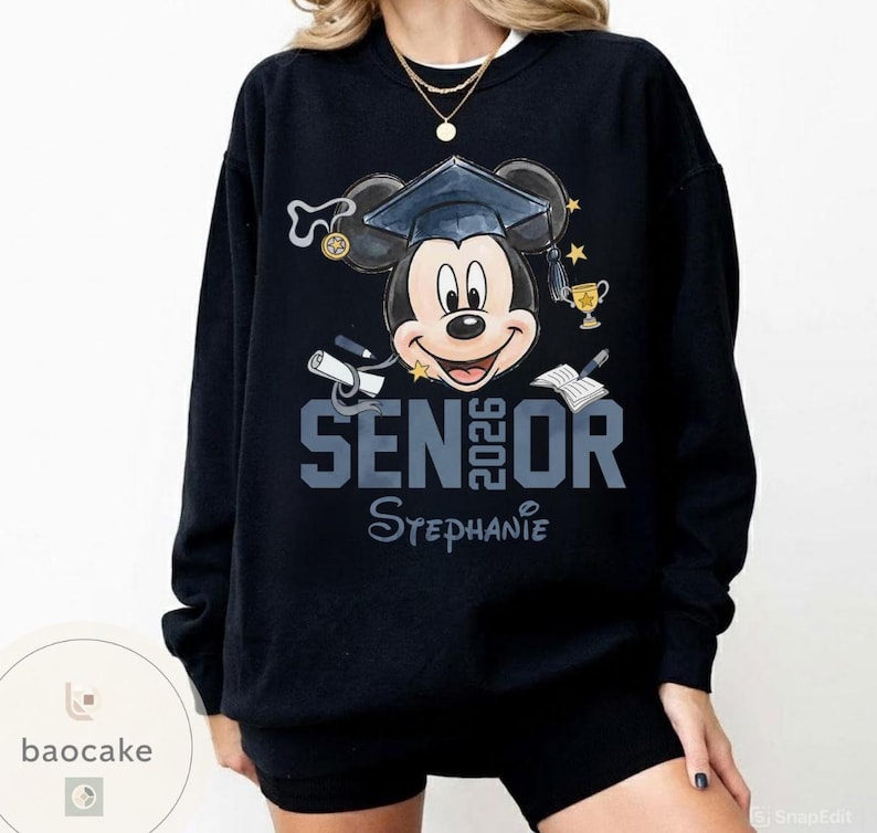May include: Black sweatshirt featuring Mickey Mouse wearing a graduation cap. The text "SENIOR 2026" is displayed in gray, with the name "Stephanie" below. The design includes graduation-themed elements like a diploma and trophy.