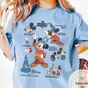 May include: Light blue t-shirt featuring Mickey Mouse as the Sorcerer's Apprentice from Fantasia. The graphic includes illustrations and text detailing the character's design, including the text "The Sorcerer's Apprentice - 1940".
