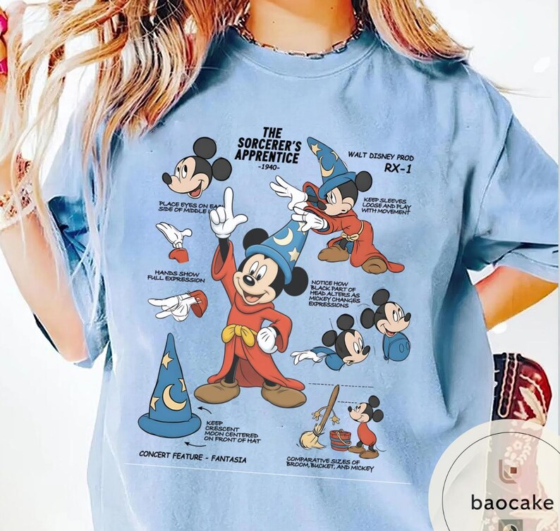 May include: Light blue t-shirt featuring Mickey Mouse as the Sorcerer's Apprentice from Fantasia. The graphic includes illustrations and text detailing the character's design, including the text "The Sorcerer's Apprentice - 1940".