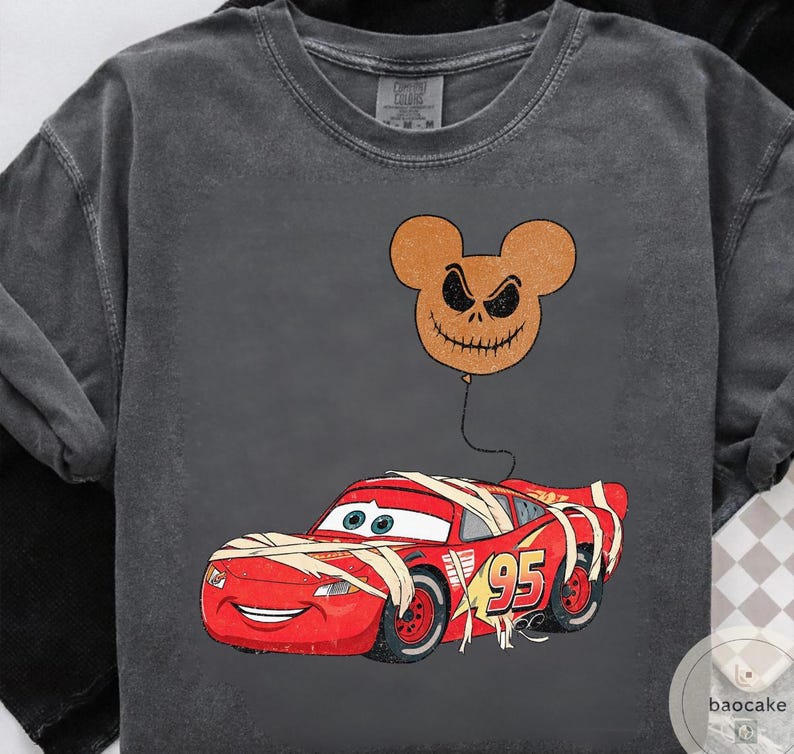 May include: Dark gray long-sleeve shirt featuring a red race car wrapped in bandages, with the number 95 on the side. A brown Jack Skellington-inspired balloon floats above the car. The shirt has a vintage, distressed look.
