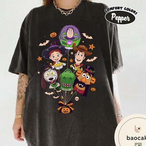 Pode incluir: Uma t-shirt cinzento-carv&atilde;o com uma impress&atilde;o gr&aacute;fica de personagens de Toy Story vestidos para o Halloween, incluindo Buzz Lightyear, Woody, Jessie, Rex, Slinky Dog e Mr. Potato Head, unidos por um la&ccedil;o e uma ab&oacute;bora de Halloween.