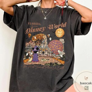 Op de afbeelding: Donkergrijze t-shirt met een Halloween-thema Disney World-afbeelding. Het ontwerp bevat Mickey Mouse in een heksenkostuum, pompoenen en de tekst "Florida Disney World" en "The Most Scariest Place On Earth."