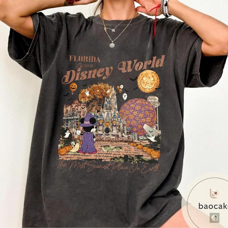 Op de afbeelding: Donkergrijze t-shirt met een Halloween-thema Disney World-afbeelding. Het ontwerp bevat Mickey Mouse in een heksenkostuum, pompoenen en de tekst "Florida Disney World" en "The Most Scariest Place On Earth."
