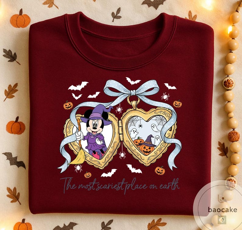 May include: A burgundy crew neck sweatshirt with a Halloween design. The graphic features Minnie Mouse as a witch, pumpkins, bats, and the text "The most scariest place on earth". A light blue ribbon is at the top of the design.
