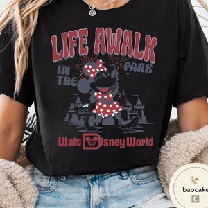 May include: Black t-shirt featuring Minnie Mouse in a red polka dot dress and bow. The shirt has the text "LIFE A WALK IN THE PARK" and "Walt Disney World" in red. A fun, vintage-style graphic tee.