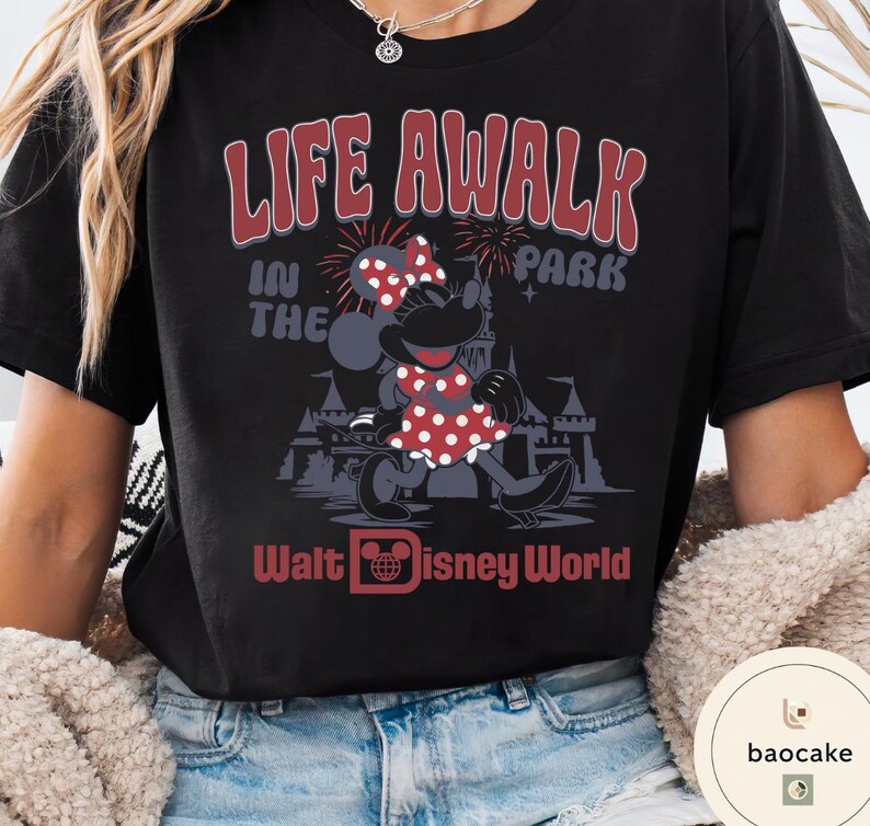 May include: Black t-shirt featuring Minnie Mouse in a red polka dot dress and bow. The shirt has the text "LIFE A WALK IN THE PARK" and "Walt Disney World" in red. A fun, vintage-style graphic tee.
