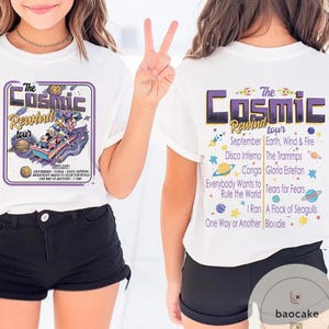 May include: White t-shirts with a graphic design. The front of the shirt features the text "The Cosmic Rewind tour" with a cartoon image. The back of the shirt lists the tour's setlist, including "September, Earth, Wind & Fire, Disco Inferno".