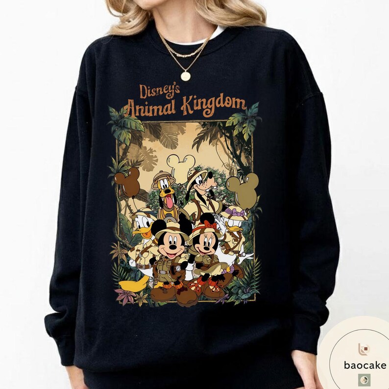 May include: Black sweatshirt featuring a graphic of Disney's Animal Kingdom characters, including Mickey and Minnie Mouse, Donald Duck, and Goofy, in safari attire. The text "Disney's Animal Kingdom" is displayed above the characters in a brown font.