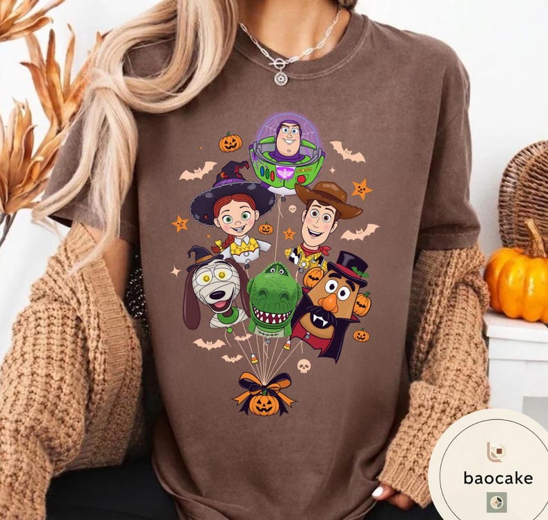 Pode incluir: Uma t-shirt castanha com uma impress&atilde;o gr&aacute;fica de personagens de Toy Story vestidos com fatos de Halloween, incluindo Buzz Lightyear, Woody, Jessie, Rex, Slinky Dog e Mr. Potato Head, atados como bal&otilde;es com uma ab&oacute;bora na base.